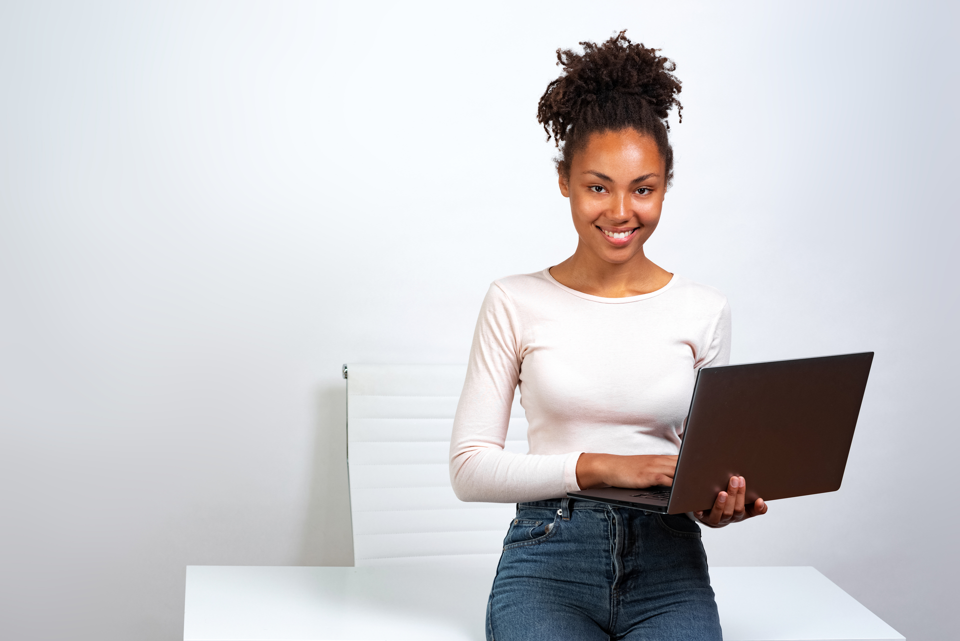 Smiling woman standing with a laptop in a bright, minimalist office setting.