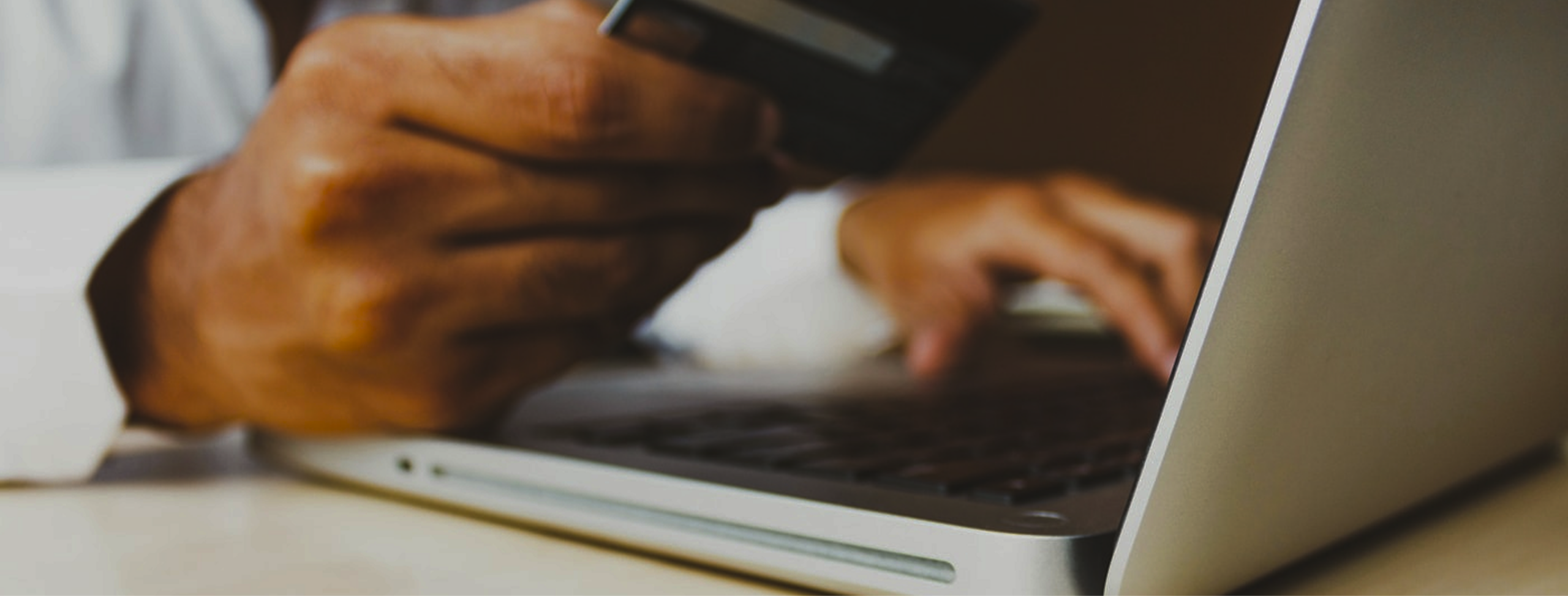 Close-up of a hand holding a credit card over a laptop keyboard, suggesting online payment.